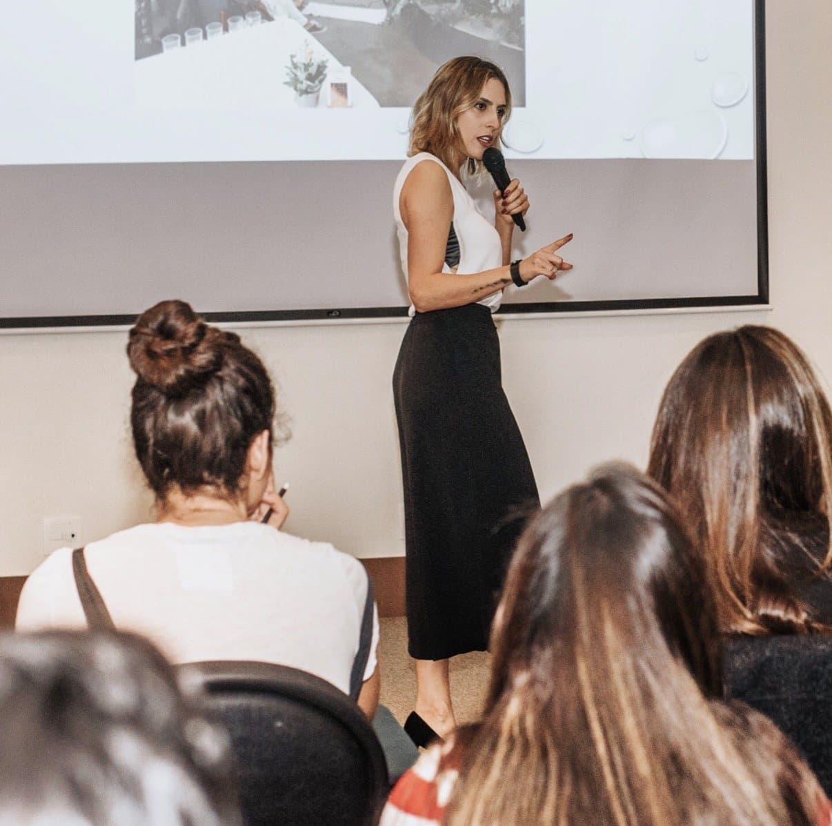 Xanda Fogaça falando ao microfone para uma plateia de mulheres
