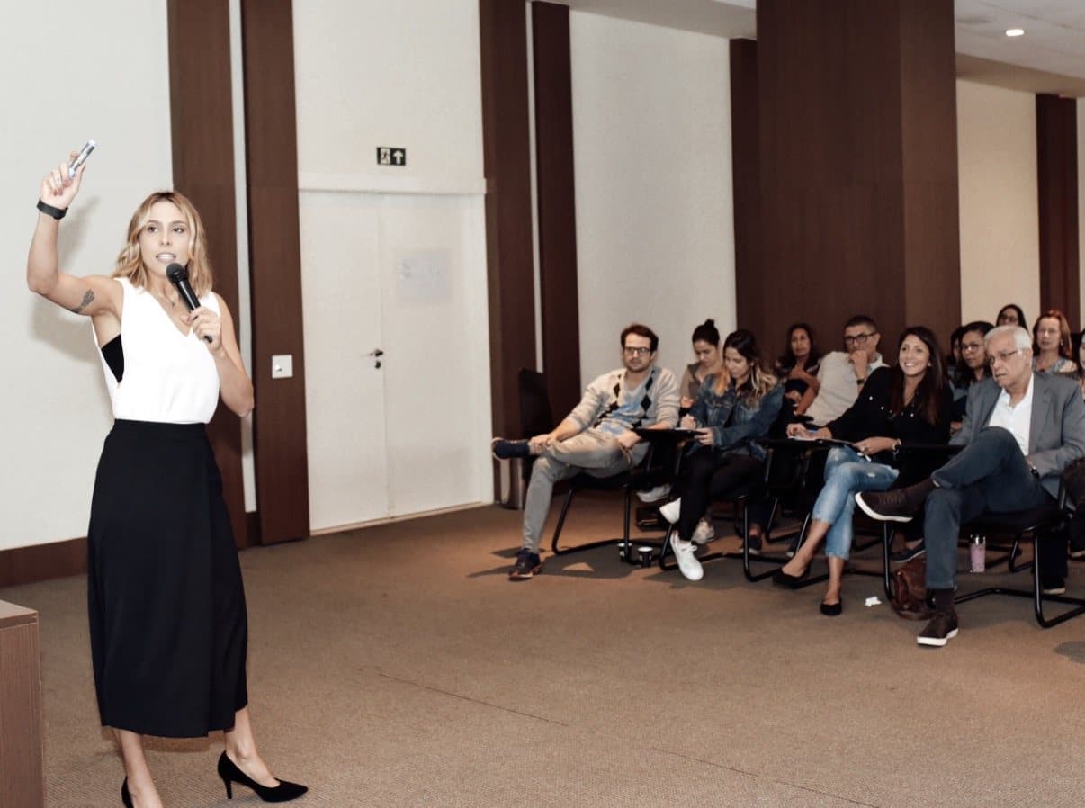 Xanda Fogaça falando ao microfone para uma plateia sentada